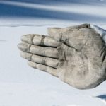 Wooden hand pointing to the left of the frame. The wooden hand sign occupies most of the frame, the ground is covered in snow.
