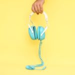 Blue headphones being held over yellow background with cord trailing.